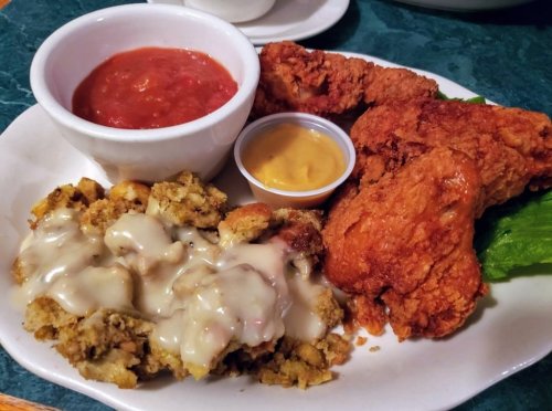 A plate featuring fried chicken, stuffing with gravy, a side of salsa, and mustard on a green lettuce leaf.