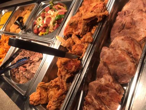 A buffet spread featuring fried chicken, sliced meats, and a colorful salad with various vegetables.
