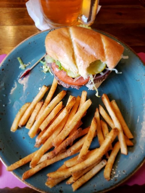 A sandwich with lettuce, tomato, and pickles on a blue plate, accompanied by a side of crispy French fries.