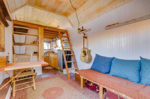 Cozy interior of a tiny house featuring a wooden loft, kitchen area, and a seating area with blue cushions.