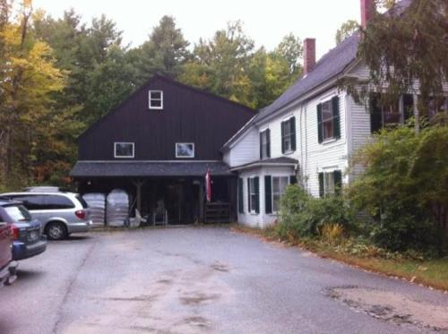 A rustic two-story building with a black upper section and white lower section, surrounded by trees and parked cars.