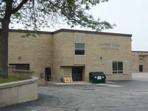 Exterior view of Brown Deer High School, featuring a brick building and a green dumpster in the parking lot.