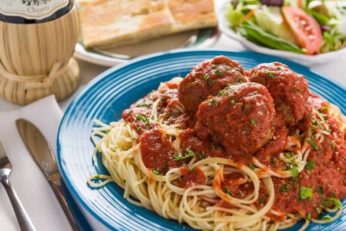 A plate of spaghetti topped with meatballs and marinara sauce, garnished with parsley, alongside a salad and bread.