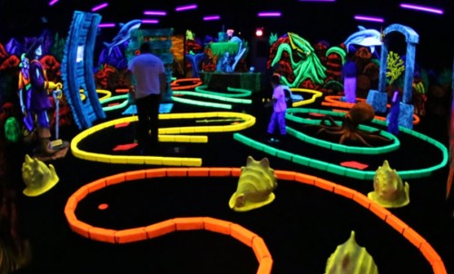 A vibrant glow-in-the-dark mini-golf course with colorful obstacles and players enjoying the game.