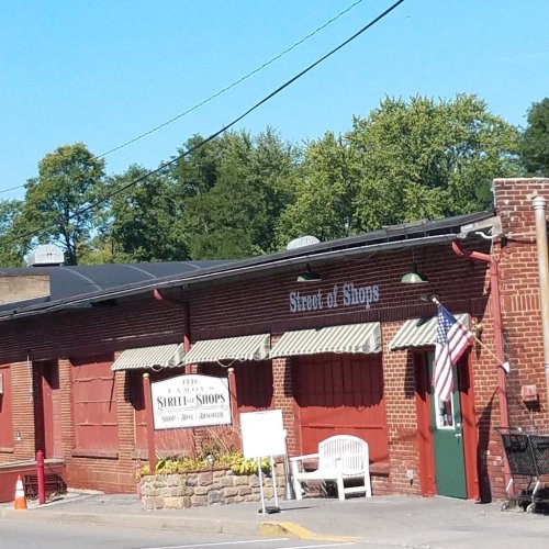 A brick building with a sign reading "Street of Shops," featuring red shutters and an American flag outside.