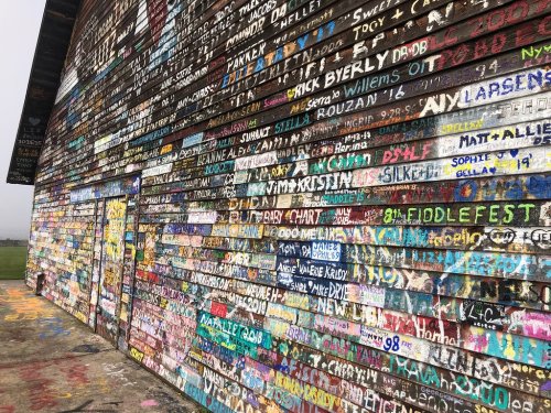 Colorful wall covered in names and messages, showcasing vibrant graffiti art in a rural setting.