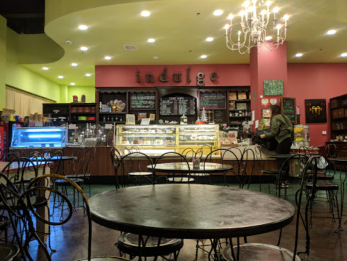 Cozy café interior with a pink wall, a display case, and tables, featuring the word "indulge" prominently.