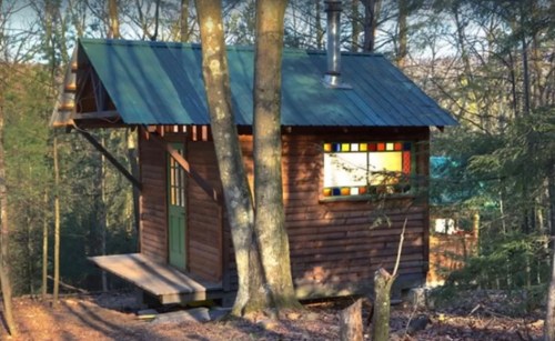 A small wooden cabin nestled between trees, featuring a green door and colorful stained glass windows.