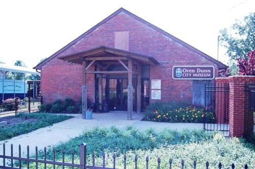 Exterior of the Oren Dunn City Museum, featuring a brick building with a wooden entrance and surrounding greenery.