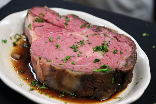 A juicy slice of prime rib on a plate, garnished with parsley and served in a savory sauce.