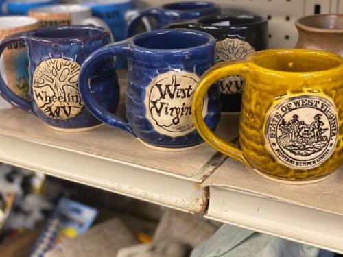 A shelf displaying colorful ceramic mugs, featuring designs related to West Virginia and Wheeling.