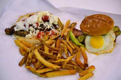A plate with a pita filled with meat, tomatoes, and feta, alongside a burger with an egg and crispy fries.