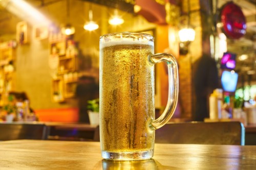 A frosty glass of beer sits on a wooden table in a warm, inviting bar setting.