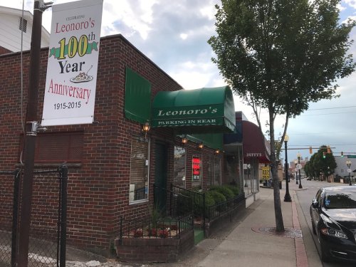 A brick building with a green awning, featuring a sign for Leonoro's 100th anniversary and nearby street views.