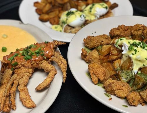 A plate featuring fried crab with sauce, poached eggs, and seasoned potatoes, alongside a bowl of creamy grits.