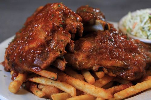 A plate of crispy fries topped with saucy ribs and a side of coleslaw.
