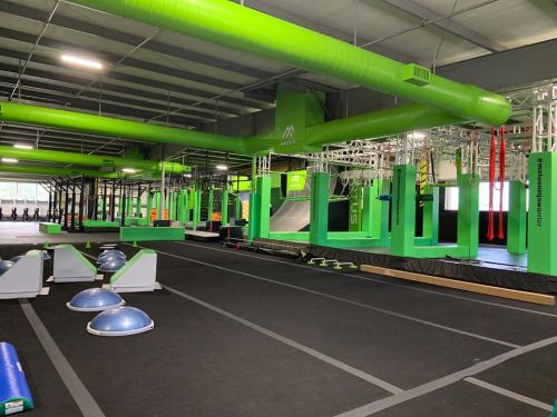 A vibrant indoor gym featuring green equipment, obstacle courses, and training areas for fitness activities.