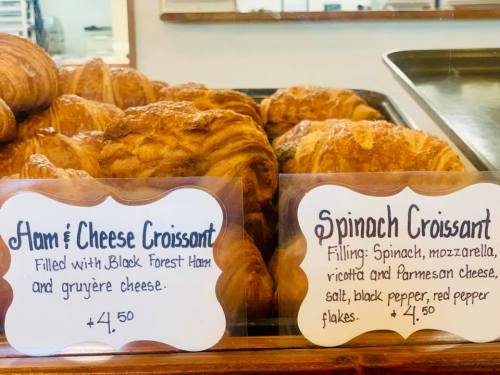 A display of croissants with signs for ham & cheese and spinach varieties, each priced at $4.50.