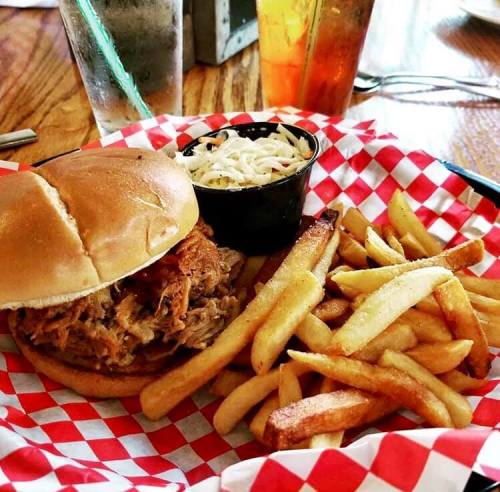 A plate with a pulled pork sandwich, coleslaw, and a side of golden fries, all served in a red-checkered basket.
