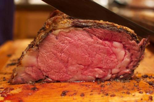Close-up of a perfectly cooked roast beef, showcasing its juicy, pink interior and crispy outer crust on a wooden cutting board.