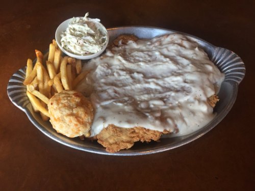 A platter featuring fried chicken smothered in gravy, served with fries, coleslaw, and a biscuit.