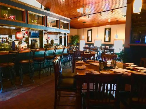 Cozy restaurant interior with wooden tables, bar area, and warm lighting, creating an inviting atmosphere.