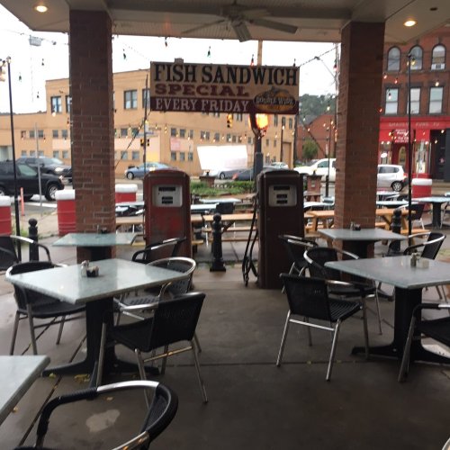 Outdoor dining area with tables, a sign for a fish sandwich special, and vintage gas pumps in the background.