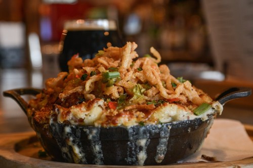 A skillet filled with cheesy macaroni topped with crispy fried onions and green onions, served in a rustic setting.