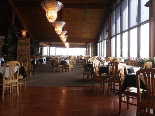 A spacious restaurant with wooden decor, elegant chandeliers, and tables set for dining, featuring large windows.