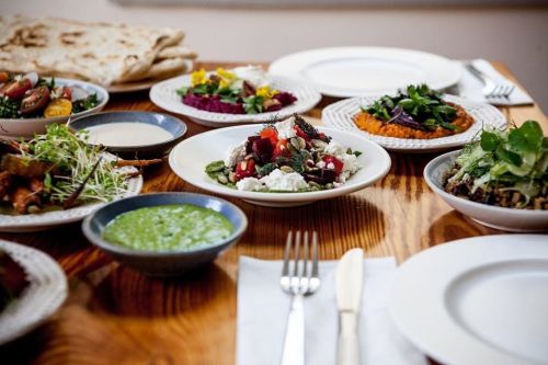 A table set with various colorful dishes, including salads, dips, and bread, arranged on white plates.