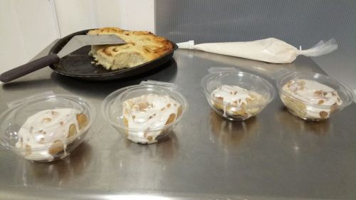 Three bowls of dessert topped with cream, alongside a tray of cinnamon rolls and a piping bag of frosting.