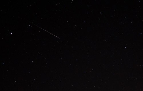 A dark night sky filled with stars, featuring a bright meteor streaking across the scene.
