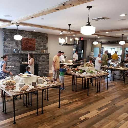 A buffet setup in a spacious room with people serving food at tables, surrounded by a cozy, rustic atmosphere.