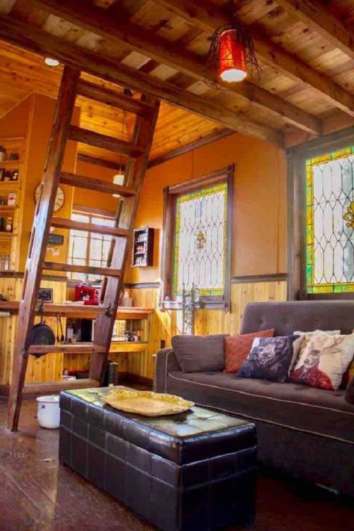 Cozy interior of a wooden cabin featuring a ladder, stained glass windows, and a comfortable sofa with decorative pillows.