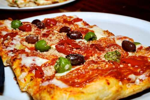 A rectangular pizza topped with pepperoni, olives, green peppers, and cheese on a white plate.