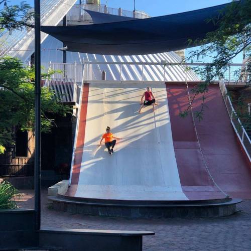Two skateboarders perform tricks on a large, curved ramp in an outdoor skate park.