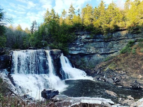 A serene waterfall cascades over rocky cliffs, surrounded by lush green trees under a clear blue sky.