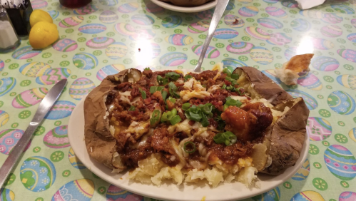 A loaded baked potato topped with chili, cheese, and green onions on a colorful patterned tablecloth.