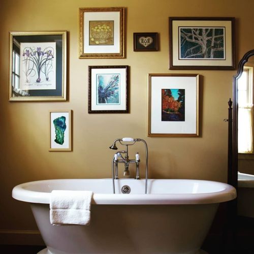 A stylish bathroom featuring a freestanding tub and a gallery wall of framed artwork in various styles.