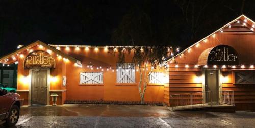 A warmly lit restaurant exterior at night, featuring the name "The Rustler" on a rustic building.