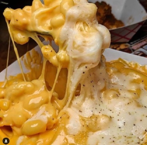 A close-up of creamy, cheesy macaroni and cheese with gooey, melted cheese stretching from the dish.