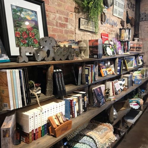 A rustic bookshelf filled with various books, magazines, and decorative items in a cozy, brick-walled setting.