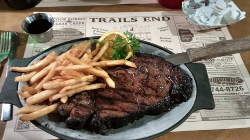 A juicy steak served on a platter with golden fries and a slice of orange, set on a rustic table with a menu.