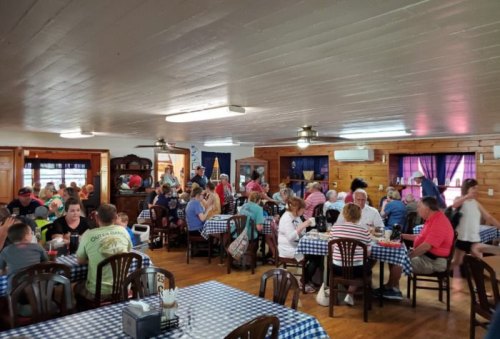 A busy restaurant interior filled with diners at tables, featuring checkered tablecloths and wooden decor.