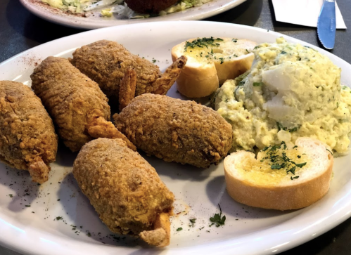 A plate of fried food featuring four breaded shrimp, a side of potato salad, and two slices of toasted bread.