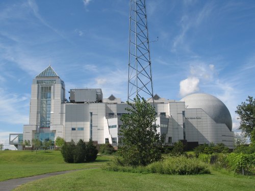 A modern building with a dome and glass features, surrounded by green grass and trees under a blue sky.