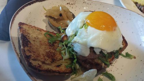 A plate featuring a toasted bread slice topped with a burger, lettuce, a poached egg, and a side of pickled onions.