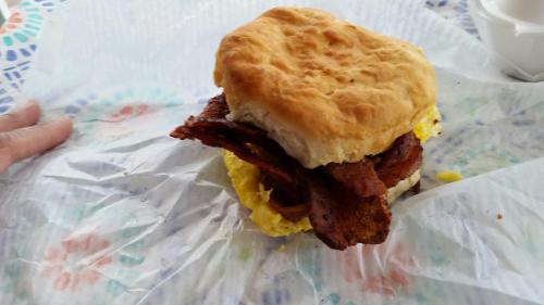 A hearty breakfast sandwich with bacon and egg, served on a fluffy biscuit, resting on parchment paper.