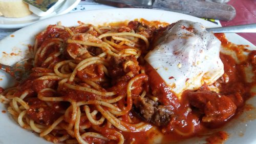 A plate of spaghetti topped with meat and a poached egg in a rich tomato sauce.