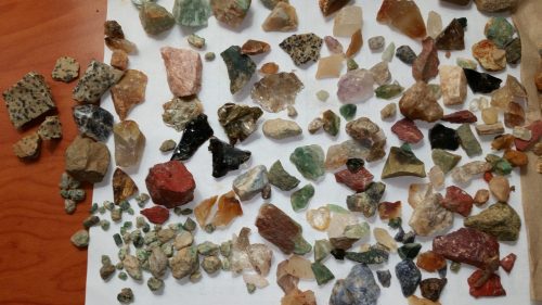 A variety of colorful gemstones and minerals scattered on a white surface, showcasing different shapes and sizes.